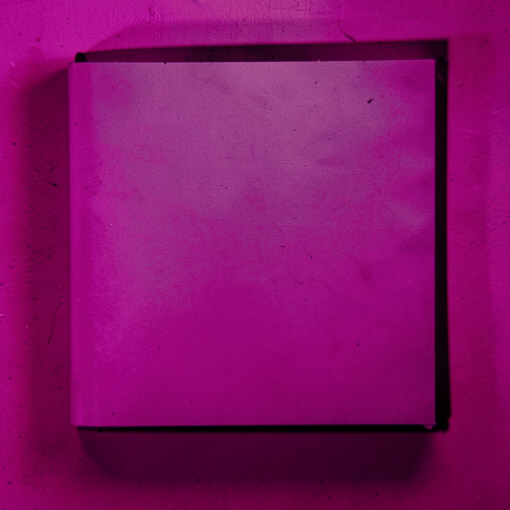 Soft pink and charcoal duotone photograph of an open notebook on a wooden desk beside a pencil, evoking a quiet guest signing space.